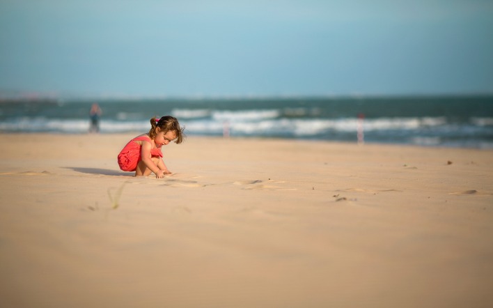 Девочка копается в песке на пляже